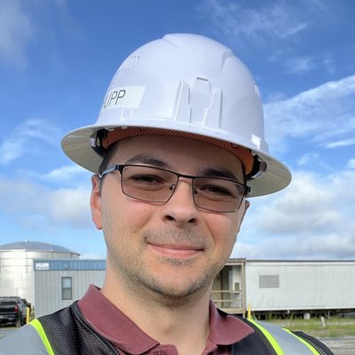 Albert on site in a hard hat and hi-vis vest, a storage tank behind him